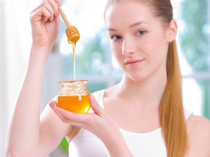 A young beautiful woman holding a small jar of honey
